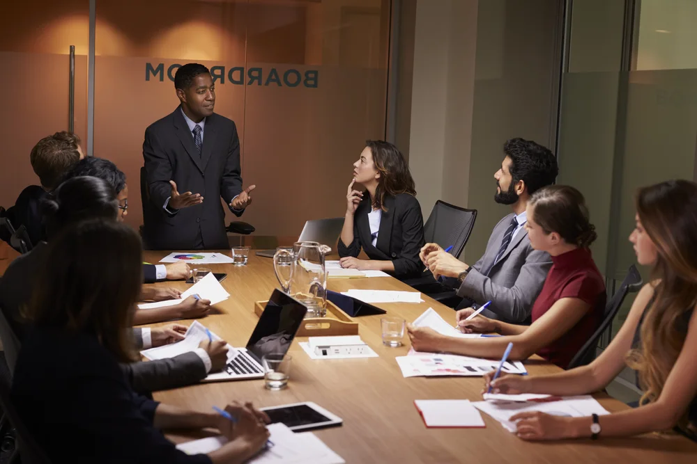 Four professionals lean together over a desk in discussion.