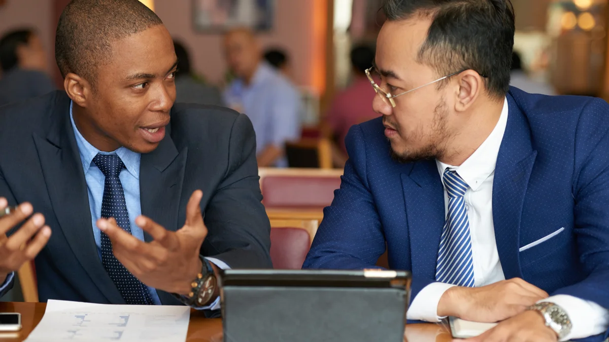 Three businesspeople discuss documents at a table.
