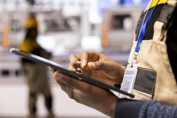 A worker uses a tablet near machinery.