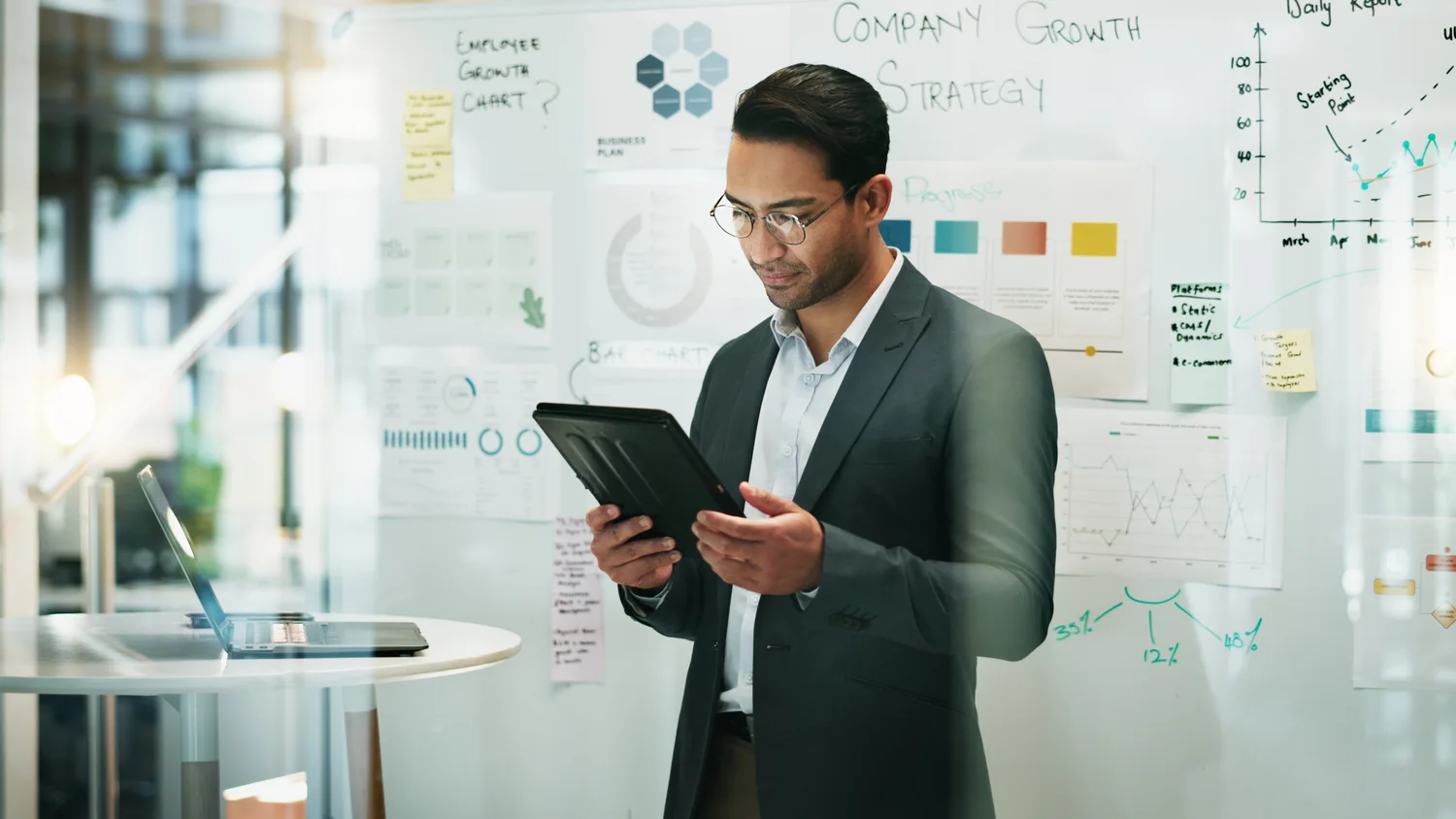 A professional reviews notes beside a glass wall covered with operational diagrams
