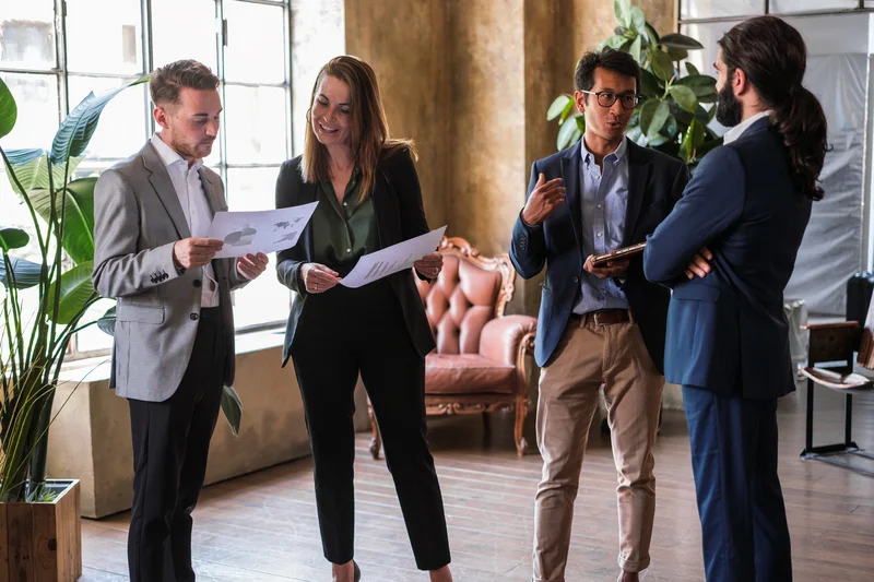 Four colleagues stand together and review a document in an office