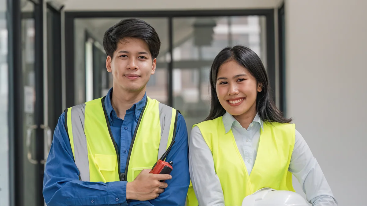 A worker and office professional pose in front of a facility sign.